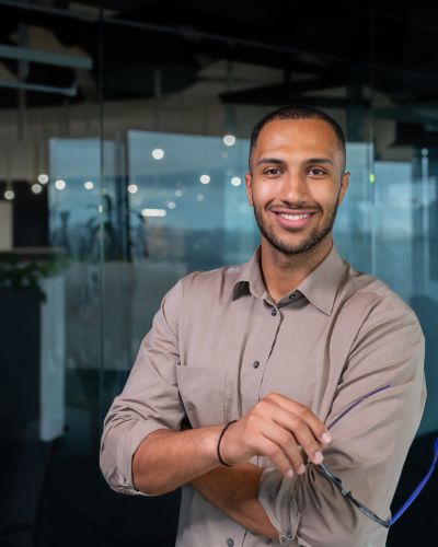 Portrait of african american businessman in office, man in shirt standing near window smiling and looking at camera, programmer working inside development company
