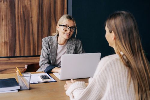 A female professional sitting at a desk in an office is interviewing a candidate for a position.
